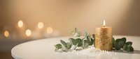 Elegant golden candle with eucalyptus leaves on white marble surface creating warm ambient lighting for spa relaxation and wellness atmosphere.