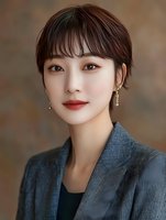 Young Asian woman with short dark hair and red lipstick wearing gray blazer against neutral background, portraying professional confidence.