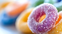 Colorful sugar-coated gummy candy rings in vibrant purple and orange hues with powdered sugar coating creating sweet confectionery macro photography.