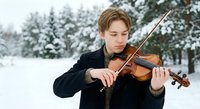 Young male violinist performing outdoors in snowy winter landscape with snow-covered evergreen trees, classical music concept for concerts and performances.