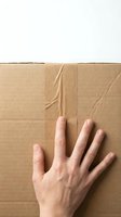 Caucasian hand placed on sealed cardboard box with tape, overhead view for shipping, delivery, and logistics concepts.