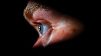 Close-up view of bright blue eye peering through dark opening, dramatic lighting creates mysterious and voyeuristic atmosphere for conceptual photography and design projects.