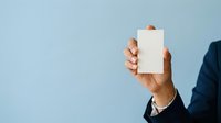 Businessman in dark suit holding blank white card against light blue background for corporate messaging and branding purposes.