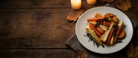 Grilled salmon fillet with roasted vegetables and rosemary garnish served on white plate with candles on rustic wooden table for fine dining and restaurant menus.