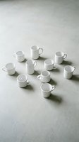 White ceramic mugs and pitcher arranged on neutral surface, casting shadows. Isolated tableware collection for product display, hospitality, kitchenware marketing, and home decor design projects.