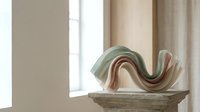 Modern abstract ceramic sculpture with flowing curves in green and pink tones displayed on marble surface in minimalist interior setting for home decor.