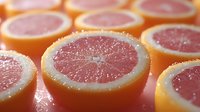Fresh pink grapefruit slices arranged in rows showing juicy pulp and rind, macro food photography with soft natural lighting and shallow depth of field.