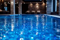 Luxurious indoor swimming pool with crystal clear blue water reflecting ambient lighting, creating a serene and elegant atmosphere in modern spa interior.