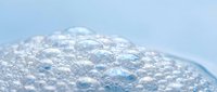 Clear soap bubbles floating on water surface with translucent foam texture creating abstract patterns for skincare and beauty product backgrounds.
