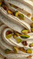 Creamy white soft serve ice cream swirls with crushed pistachio nuts scattered throughout, macro food photography showing rich texture and natural ingredients.