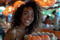 Young African American woman with curly hair smiling brightly while enjoying sushi rolls at restaurant with warm ambient lighting and bokeh background. Casual dining atmosphere.