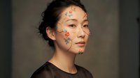 Young Asian woman with colorful floral face paint featuring delicate flowers and leaves in artistic makeup design for beauty and creative expression.