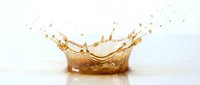 Golden liquid splash creating crown-shaped formation with droplets against white background. Dynamic fluid motion for beverage advertising and design projects.