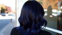 Dark blue-black wavy hair styled in modern shoulder-length cut shown from behind, demonstrating professional hair coloring and styling technique in salon setting.