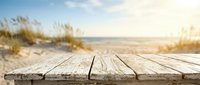 Wooden boardwalk deck overlooking sandy beach with dune grass and ocean horizon at sunset, suitable for travel and vacation marketing.