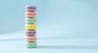 Colorful French macarons stacked in tower on pastel blue background. Sweet dessert cookies in rainbow colors for bakery menu and confectionery advertising.