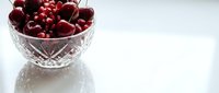 Fresh dark red cherries in crystal bowl on white surface with reflection, suitable for food photography, culinary blogs, recipe websites, and healthy eating content.