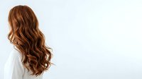 Woman with long wavy auburn hair styled in loose waves, shown from behind wearing white clothing against neutral background for hair care and beauty campaigns.