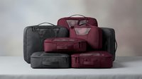 Professional packing cubes and travel organizers in burgundy and black colors arranged on neutral background for luggage organization and storage.