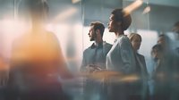 Diverse business professionals in modern glass office environment with soft light effect creating atmospheric corporate scene.