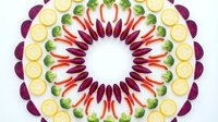 Fresh vegetables arranged in colorful mandala pattern with radishes, broccoli and onions creating decorative circular design for healthy eating concepts.