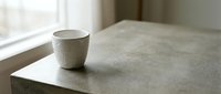 Minimalist ceramic cup on concrete surface near window with natural light, suitable for home decor and lifestyle design projects.