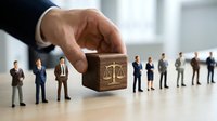 Business hand selecting wooden cube with justice scales icon from row of miniature professional people figures representing legal recruitment and law firm staffing.