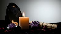 Mystical altar setup with burning candle, amethyst crystals, ancient scroll and black obsidian mirror for spiritual rituals and divination practices.
