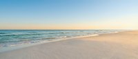 Serene ocean waves gently washing onto pristine sandy beach during golden hour sunset with soft pastel sky colors creating peaceful coastal atmosphere.