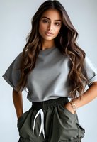 Young mixed race woman with long wavy brown hair wearing casual gray t-shirt and olive green joggers against white background, fashion portrait with natural makeup look.