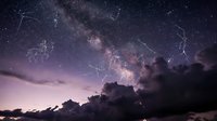 Stunning night sky with Milky Way galaxy and constellation patterns visible above dramatic cloud formations creating magical stargazing scene for astronomy content.