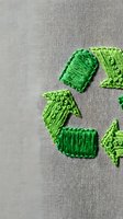 Green embroidered recycling symbol on beige fabric texture showcasing environmental awareness and sustainability concept for eco-friendly design projects.