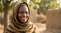 Smiling African woman wearing traditional brown patterned headscarf in rural village setting with warm natural lighting and cultural authenticity.