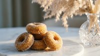 Fresh baked cinnamon sugar donuts stacked on plate with pampas grass decoration in warm natural light for bakery cafe restaurant menu design.