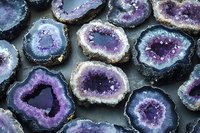 Purple amethyst geode slices with crystallized centers displaying natural concentric patterns and varying shades from deep violet to light blue on dark background.