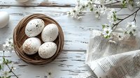Fresh speckled eggs in rustic woven basket with spring cherry blossoms and vintage newspaper on white wooden background, perfect for Easter holiday design, food blog, or seasonal marketing.