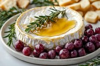 Baked camembert cheese with honey drizzle, fresh rosemary sprigs and red grapes on white ceramic plate, served with bread cubes for dipping. Appetizing party snack.