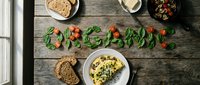 Organic breakfast flatlay on rustic wooden table with herb omelette, whole grain toast, mushrooms, and the word organic spelled with fresh vegetables.