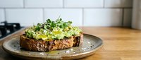 Avocado toast topped with microgreens and seeds on rustic bread served on ceramic plate in modern kitchen setting for healthy breakfast or brunch meal.