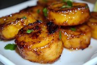 Caramelized pineapple rings grilled with honey glaze and garnished with fresh herbs on white plate, showing charred edges and glossy surface texture.