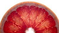 Sliced grapefruit half showing vibrant red flesh and natural citrus segments, isolated on white background for food and beverage design use.