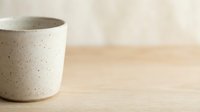 Minimalist ceramic cup with speckled glaze sitting on wooden surface, ideal for beverage, kitchenware, and home decor design projects.