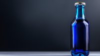Vibrant cobalt blue glass bottle with metal cap on dark background, dramatic side lighting creates elegant reflection on glossy surface. Minimalist beverage presentation.