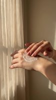 Woman applying white moisturizing cream on hands in soft natural sunlight for daily skincare routine and hydration.