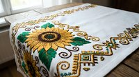 White linen table runner with embroidered sunflower and geometric folk art design on wooden dining table for home decor and traditional crafts.