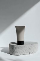 Minimalist cosmetic tube on concrete podium with dramatic shadow casting. Clean modern composition for beauty and skincare product presentation.