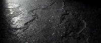 Wet asphalt road surface with cracks and water reflections after rain, dark pavement texture background for urban transportation concepts.