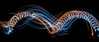 Abstract light trails forming flowing wave patterns in blue and orange neon colors against black background, suitable for modern design, technology, and motion graphics projects.