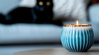 Glowing turquoise ceramic candle holder with burning flame on blurred background, creating cozy atmosphere for relaxation and meditation at home.