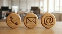 Wooden contact icons on desk showing phone, email and at symbol for business communication and customer service in modern office environment.